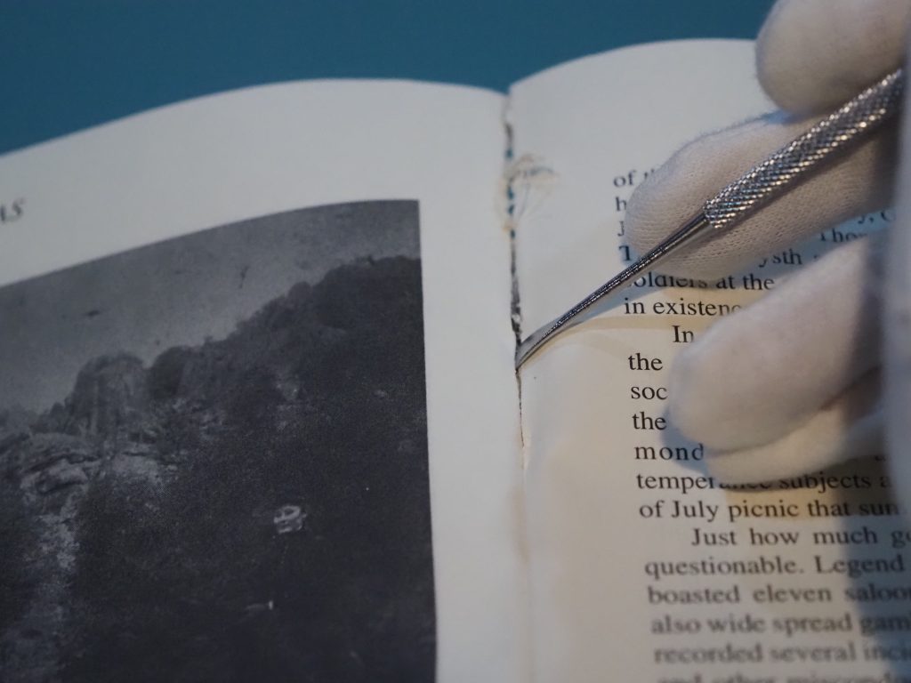 Open book with white gloved hand holding jewelr scraping tool to pull apart pages gently